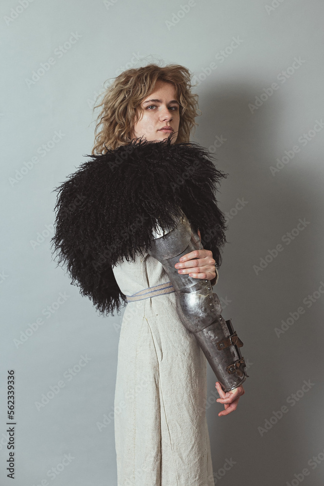 Poster curly haired woman with metal armour on arm in studio portrait picture. side view photography with l