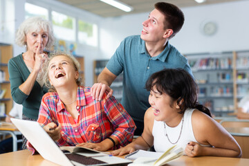 Mature European teacher woman asks amused schoolchildren to behave a little quieter, who are preparing for classes in the school library
