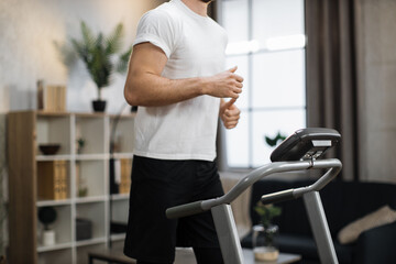 Obraz na płótnie Canvas Concept of health and morning workout. Close up view of part of body of young sportsman running on treadmill on the background of modern stylish house.