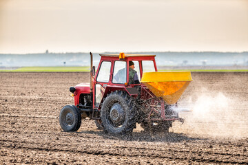 A farmer in an agricultural tractor at a farm fertilizing an arable field, a crucial step in crop...