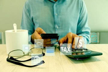 Businessman holding a smartphone and calculates taxes with a calculator, mug of coffee, and eyeglasses on the wood table. Text icon on screen.