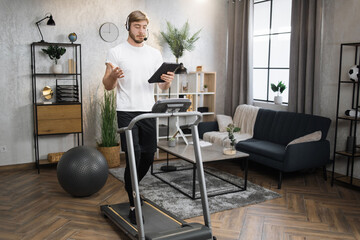 Full length handsome caucasian businessman in headset exercising with tablet, having workout on a...