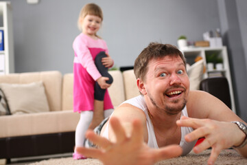 Little smiling girl holds father the leg, is lying on floor