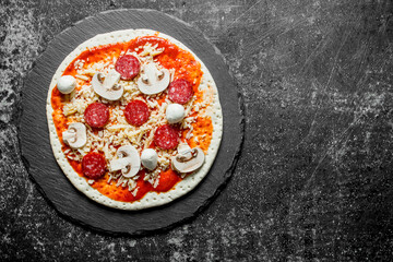 Raw pizza with sausages and mushrooms on a stone Board.