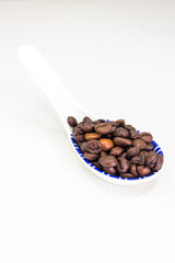 Roasted coffee beans in a spoon laying on white background