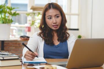 Asian people study online course via internet. Young girl watching business lesson from laptop computer and note lecture to notebook at home.