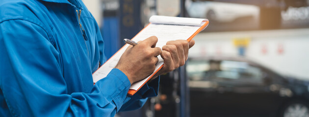Auto check up and car service shop concept. Mechanic writing job checklist to clipboard to estimate...