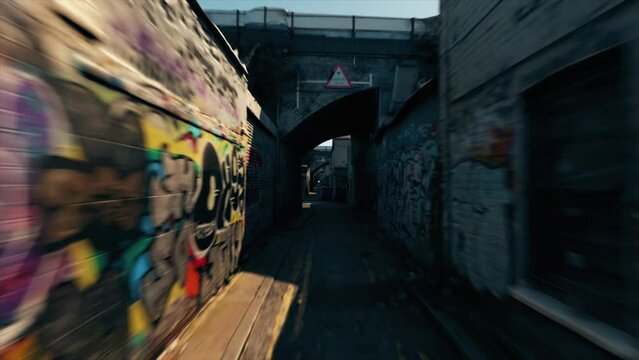 Abandoned city street. Lots of colorful graffiti on the walls. Trashcan. Road sign. Bridge. Sunny day. Movement back