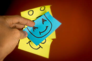hand holding a smiling yellow sticky note. different expressions blurred concept blurred concept. dim light