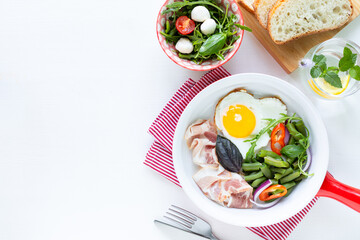 European breakfast: heart shaped egg, bacon, green beans on a white table. Selective focus. View from above. Copy space