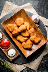 Chicken nuggets in a plate on a stone Board with paper and different sauces.