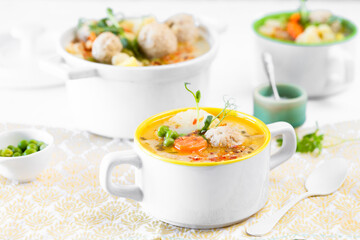 Soup with meatballs, cauliflower, baby peas, carrots and cream on a white background.