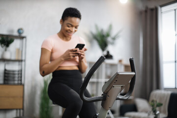 Fototapeta na wymiar Focus on screen connected online to live streaming subscription service for biking exercise. Low angle view of african female cyclist, exercising at home, riding stationary bike simulator.