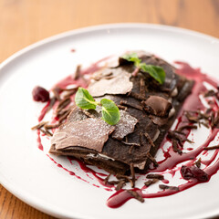 Chocolate dessert with cherry sauce on white plate, decorated with mint. View from above. Serving dish.