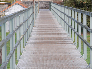 Fototapeta na wymiar Perspektive Sicht auf eine Fußgängerbrücke mit Stahlgeländer und Gitterrost zur Überquerung einer Überschwämmungsfläche
