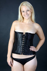Beautiful blonde woman wears black corset or corsage as lingerie or underwear in studio