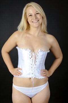 Happy smiling blonde woman wears white corset or corsage as lingerie or underwear in studio