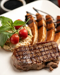 Grilled meat steak with side dish on white plate. Side dish of baked potatoes, cherry tomatoes, and vegetable salad. Soft focus. Photos for menu. 