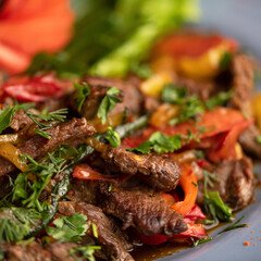 Fried meat with vegetables and herbs. Fried pieces of beef with pepper, tomato, parsley and dill. Warm salad with beef. Dish on plate. Close-up. Soft focus.