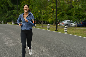 Happy asian woman in sportswear and earphones jogging in a green park. Healthy lifestyle, workout and wellness concept