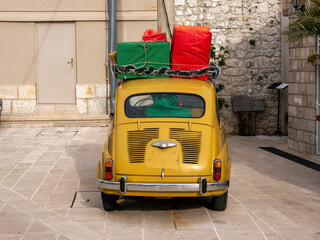 Little yellow vintage car with red, green and yellow gift boxes on its roof back view