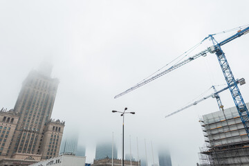 European city Warsaw with the Palace of Culture and construction cranes are building a building in...