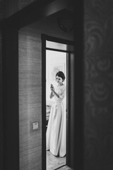 View of bride in dress through door. Beauty of bride wearing fashion wedding dress, studio photo. Attractive model. Black and white photo.