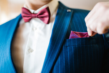 The man corrects handkerchief on the suit. The groom in a suit, shirt with bow-tie. Close up. Expensive suit, bow tie and elegant handkerchief. - obrazy, fototapety, plakaty