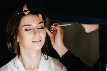 Make-up artist applying bright color eyeshadow on model's eye and holding a brush on background, close up. Young beautiful woman.