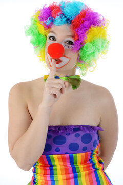 Clown in colorful costume in studio in front of white background holds finger in front of mouth and makes shush