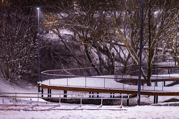 Winter park in the evening covered with snow with a row of lamps