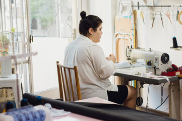 young woman sitting in her sewing workshop preparing the sewing machine to work.