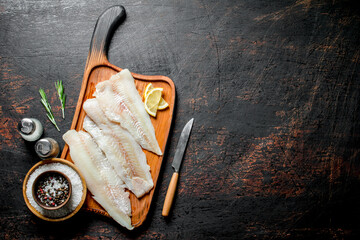 Fish fillet on a cutting Board with slices of lemon, oil and spices.