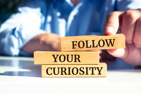Close up on businessman holding a wooden block with "Follow your Curiosity" message