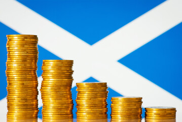 Downcomming graph made of gold coins against flag of Scotland. Concept of inflation in Scotland, low gdp rate