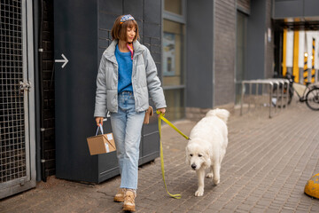 Young woman walks with her dog carrying a parcel received from automatic post office machine on a street outdoors. Concept of modern technologies in self delivery services and lifestyle