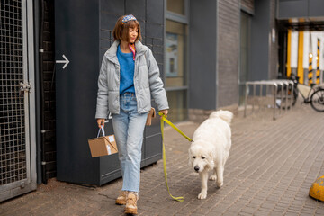 Young woman walks with her dog carrying a parcel received from automatic post office machine on a...