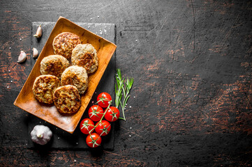 Cutlets on a wooden plate with garlic,rosemary and tomatoes on a branch.