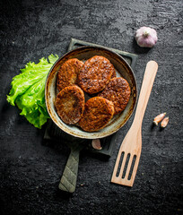 Cutlets in pan with garlic,salad leaves and a wooden shovel.