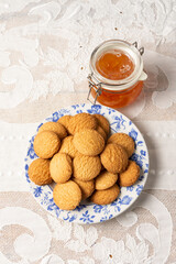 Overhead view of plate of cookies and jar of jam on table with white tablecloth, vertical, white background, with copy space