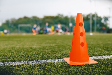 Plastic training cone on football pitch. Soccer training equipment on artificial grass field. Red practice cone standing on sideline