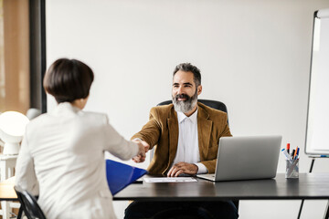 A businessman is shaking hands with future associate while sitting at the office in company.