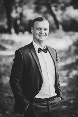 Groom in a suit with a bow tie. Groom at tuxedo smiling. Rich groom at wedding day. Black and white photo.