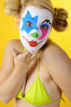 Ugly horror clown celebrates halloween or carnival in bikini gives an air kiss
