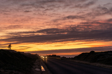 Sunset over the Remédios viewpoint in Peniche, with cars with their headlights on on the road.