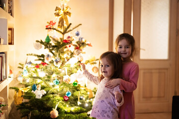 Obraz na płótnie Canvas Two sisters together near Christmas tree at evening home.