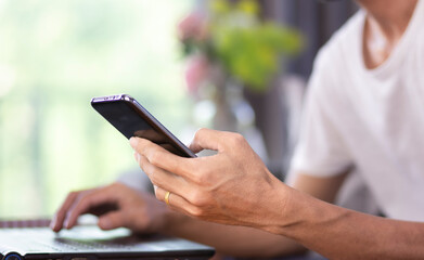 Close-up hand of man or student using smartphone and work with laptop at home