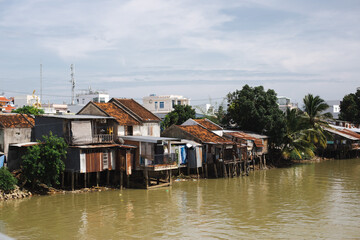 Fototapeta na wymiar Poor and old houses on the water near a dirty river in Asia, Vietnam against the backdrop of a mountain on a sunny day