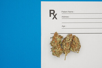Dry cannabis buds flower over the medical prescription sheet on a blue background