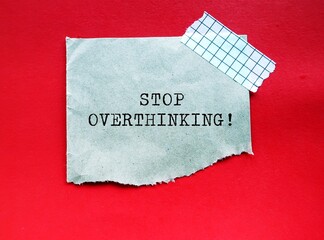 Torn note on red background with handwritten text STOP OVERTHINKING, to remind self to stop...